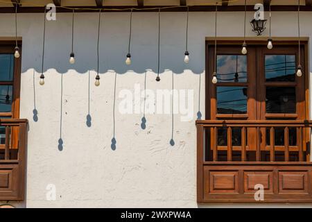 Einige hängende Glühbirnen werfen am Nachmittag ihren Schatten auf eine weiße Wand in der Kolonialstadt Villa de Leyva in Zentral-Kolumbien. Stockfoto