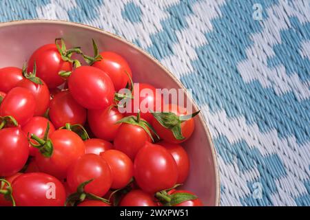 Eine Schüssel mit frischen Bio-Tomaten auf gewebtem Hintergrund mit geometrischen Mustern in Grün und weiß. Stockfoto