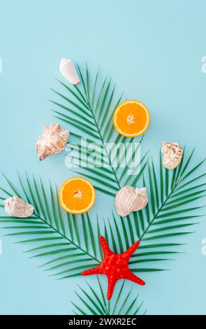 Tropisches Strandkonzept mit grünen Palmenblättern, roten Seesternen, Orangenfrüchten und Muscheln auf pastellblauem Hintergrund. Minimalistisches Design für den Sommer. Stockfoto