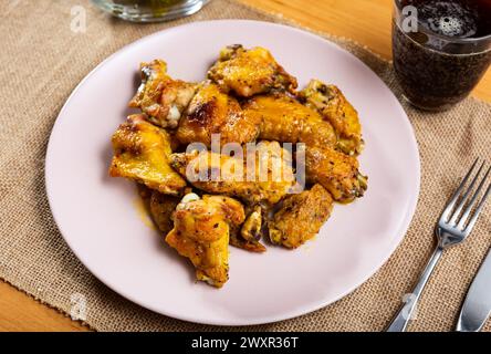 Es gibt einen herzhaften Snack auf dem Teller - eine große Portion gebratener Hähnchenflügel mit eingelegten Gurken. Stockfoto