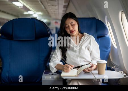 Eine attraktive und elegante asiatische Geschäftsfrau ist in der Business Class in einem Flugzeug und fliegt zu einem Geschäftstreffen in eine andere Stadt. Menschen und Transportation Stockfoto