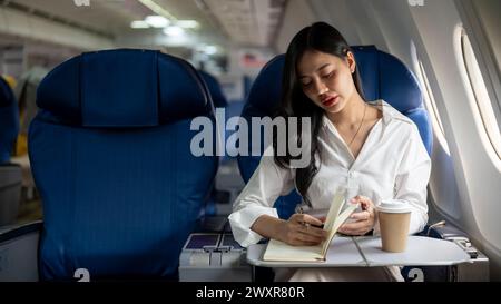 Eine attraktive und elegante asiatische Geschäftsfrau ist in der Business Class in einem Flugzeug und fliegt zu einem Geschäftstreffen in eine andere Stadt. Menschen und Transportation Stockfoto