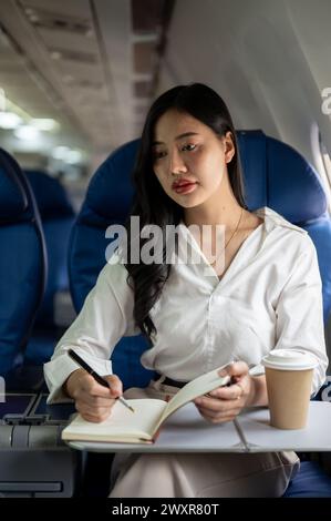 Eine attraktive und elegante asiatische Geschäftsfrau ist in der Business Class in einem Flugzeug und fliegt zu einem Geschäftstreffen in eine andere Stadt. Menschen und Transportation Stockfoto
