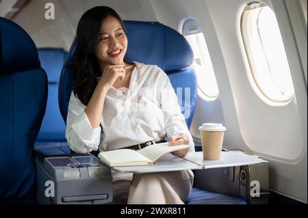 Eine attraktive asiatische Geschäftsfrau blickt auf den Blick außerhalb des Fensters, sitzt an einem Fenstersitz im Flugzeug und geht auf Geschäftsreise. Geschäftsleute Stockfoto