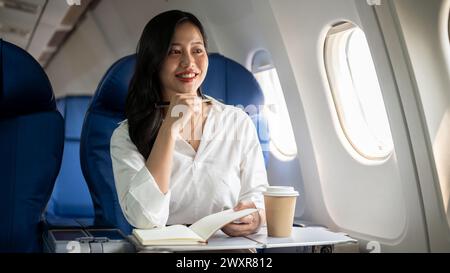 Eine attraktive asiatische Geschäftsfrau blickt auf den Blick außerhalb des Fensters, sitzt an einem Fenstersitz im Flugzeug und geht auf Geschäftsreise. Geschäftsleute Stockfoto