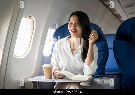 Eine attraktive asiatische Geschäftsfrau blickt auf den Blick außerhalb des Fensters, sitzt an einem Fenstersitz im Flugzeug und geht auf Geschäftsreise. Geschäftsleute Stockfoto
