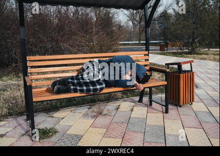 Obdachloser alter Mann liegt im Herbst auf einer Parkbank Stockfoto