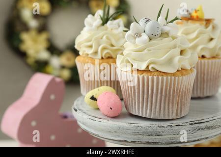 Leckere Ostercupcakes mit Vanillecreme und Süßigkeiten auf Kuchenständer, Nahaufnahme Stockfoto