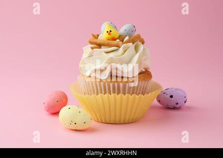 Leckerer Ostercupcake mit Vanillecreme und Süßigkeiten auf rosa Hintergrund Stockfoto