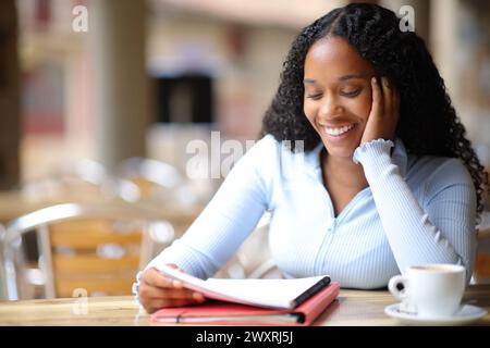 Glückliche schwarze Studentin, die Notizen auf der Terrasse eines Coffee-Shops auswendig macht Stockfoto