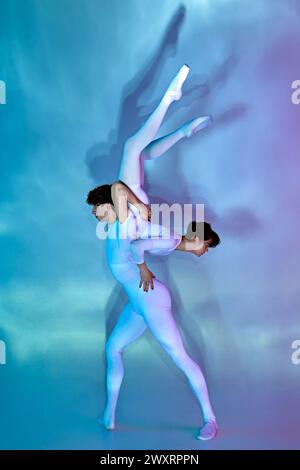 Ein männlicher Balletttänzer hebt seinen Partner in einer anmutigen Tanzposition, die von violettem und blauem Licht vor verlaufendem Hintergrund umrahmt wird. Stockfoto