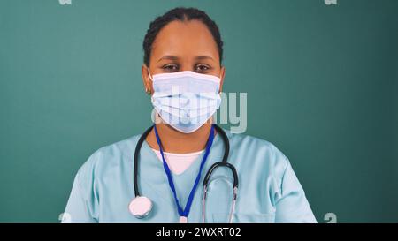 Junger schwarzer Arzt in Peelings mit blauer chirurgischer Gesichtsmaske, Operationsvorbereitung Stockfoto