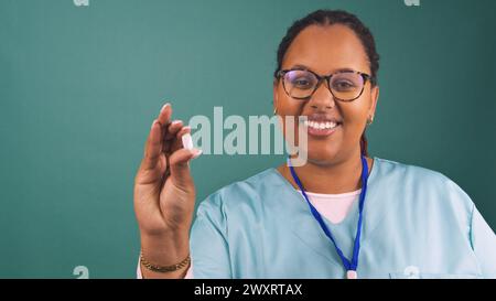 Die junge schwarze Krankenschwester spricht und hält die Pille, lächelt in blauem Gewächs Stockfoto