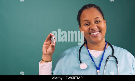 Junge schwarze Ärztin spricht mit Impfstofffläschchen und lächelt in blauen Peelings Stockfoto