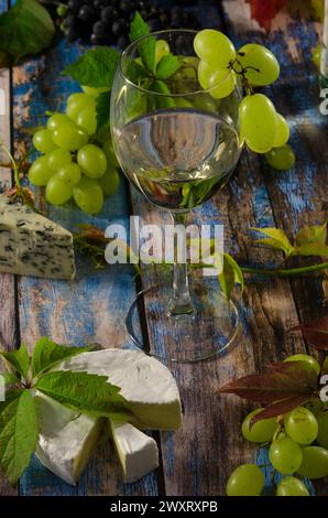 Glas Weißwein auf blauem Holzhintergrund mit Trauben und Blauschimmelkäse. Stockfoto