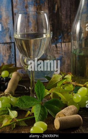 Glas Weißwein auf hölzernem Hintergrund mit Trauben, Blättern und Weinkorken. Stockfoto