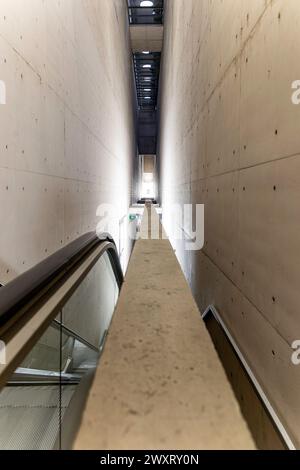 Ein langer, schmaler Flur mit einer Betonmauer. Die Wand ist mit kleinen Löchern bedeckt und hat eine graue Farbe. Der Flur ist leer und hat keine Personen oder Gegenstände Stockfoto
