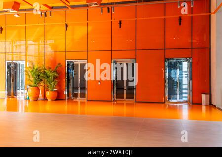 Aufzüge in orangefarbenem, glänzenden Hallenboden mit Pflanzen im Innenbereich. Stockfoto