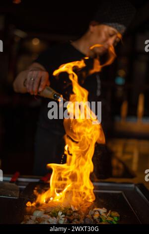 Berlin, Deutschland 08. 16. 2023. Der Teppanyaki-Koch kocht im Teppan in einem japanischen Steakhaus. Der japanische Koch zeigt eine Show mit Feuer und Flambé Stockfoto