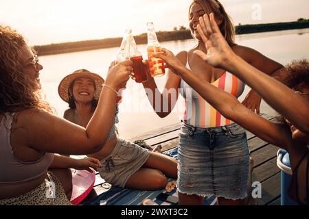 Eine junge Frau, die ihren Freunden Drinks bringt, die auf dem Pier am See sitzen. Stockfoto