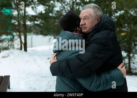 Niedliches pensioniertes Paar, das im Park spaziert und sich im Winterpark umarmt Stockfoto