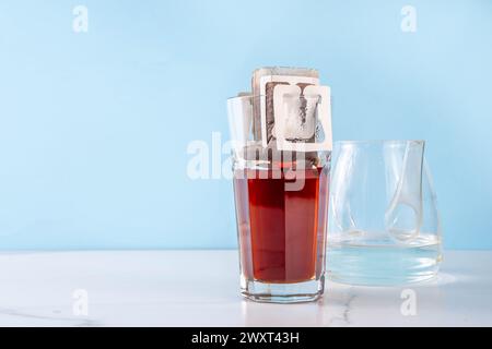 Moderne schnelle Instant-Tasse frisch gebrühten Kaffee, tropfgebrühter Beutel frischer Kaffee Espresso in Glasbecher. Frauenhände gießen Wasser in Kaffeefilterbeutel Stockfoto