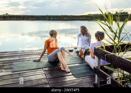 Gruppe von älteren Frauen, die auf Yogamatten sitzen und nach dem Training sprechen. Stockfoto
