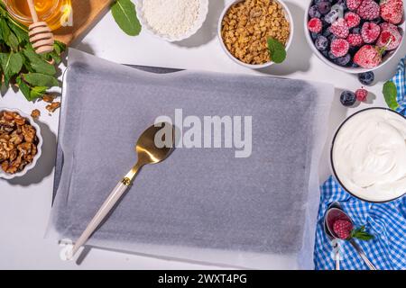 Kochen Herstellen gefrorener Joghurtrinde Hintergrund mit griechischem Joghurt, frischer Beere, Müsli, Honig, Schokoladensauce, mit Backblech Deko. Blick von oben auf die Frau Stockfoto