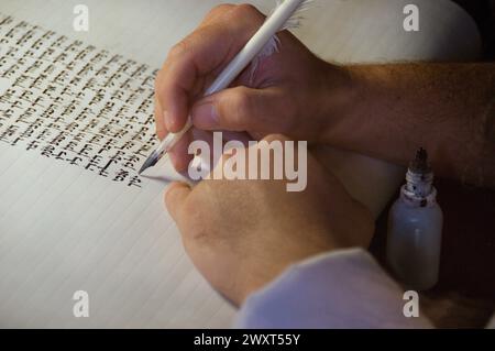 Nahaufnahme der Hände eines jüdischen Schriftstellers, der den hebräischen Text der Thora oder Bibel auf Pergament mit Federfeder und schwarzer Tinte schreibt. Stockfoto