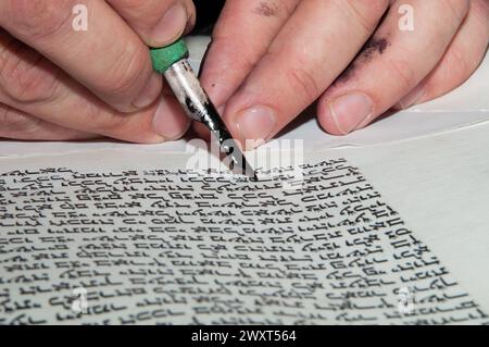 Nahaufnahme der Hände eines jüdischen Schriftstellers, der den hebräischen Text der Thora oder Bibel auf Pergament mit Federfeder und schwarzer Tinte schreibt. Stockfoto