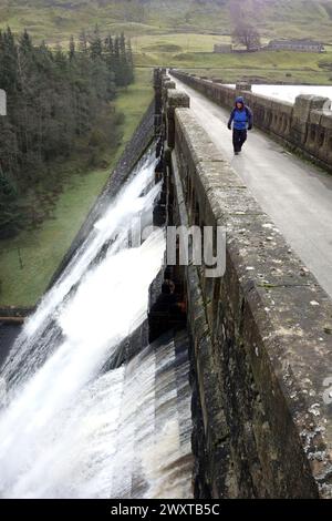 Man (Wanderer) geht über den Ausfluss am Stone Dam Wall of Scar House Reservoir in Nidderdale, Yorkshire Dales National Park, England, Großbritannien. Stockfoto