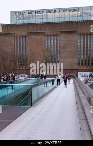 Menschen auf der Millennium Bridge vor der Galerie Tate Modern, auf der der Slogan „See Great Art from the Around the World“ zu sehen ist Stockfoto