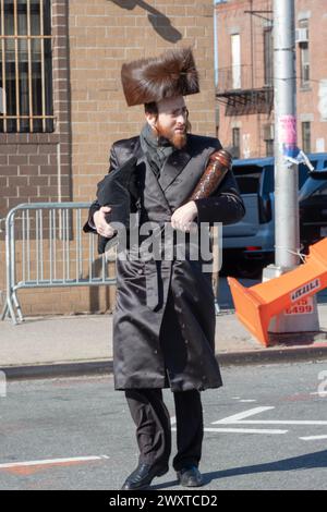 Ein orthodoxer jüdischer Mann kehrt aus dem Tempel auf Purim zurück, trägt einen Schtreimel-Pelzhut und trägt eine tallis-Tasche und Megillah. In Brooklyn, New York. Stockfoto