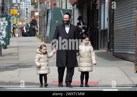 Ein chassidischer jüdischer Vater und seine gleichgekleideten Töchter überqueren eine Straße in Brooklyn, New York. Stockfoto