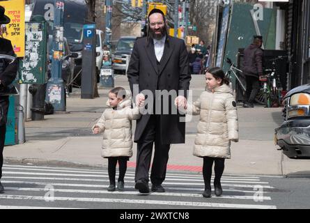 Ein chassidischer jüdischer Vater und seine gleichgekleideten Töchter überqueren eine Straße in Brooklyn, New York. Stockfoto