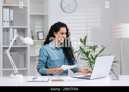Inhalt Hispanic Frau, die Papierarbeit in einem gut organisierten Home Office-Umfeld verwaltet und Professionalität und Positivität ausstrahlt. Stockfoto