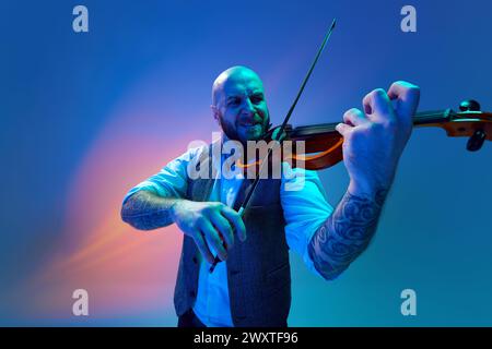 Intensive Melodie. Künstlerischer Glatzmann, Musiker, der Geige vor blauem Hintergrund in Neon mit gemischtem Licht spielt Stockfoto