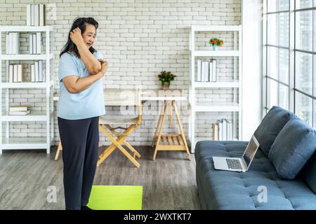 Eine asiatische Frau, die die Trainingsschritte eines Videos wiederholt, das auf dem Laptop abgespielt wird Stockfoto