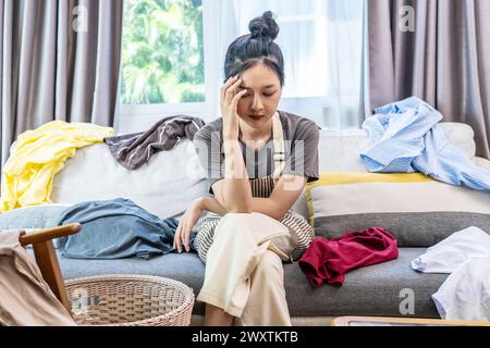 Eine Frau, die Kopfschmerzen hat, wegen der dreckigen Wäsche im ganzen Zimmer Stockfoto