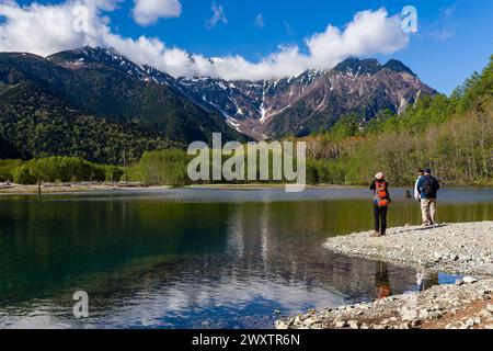 KAMIKOCHI, JAPAN - 24. MAI 2023: Wanderer neben einem Teich und dem Fluss Azusa mit schneebedeckten Bergen dahinter. Kamikochi, Präfektur Nagano Stockfoto