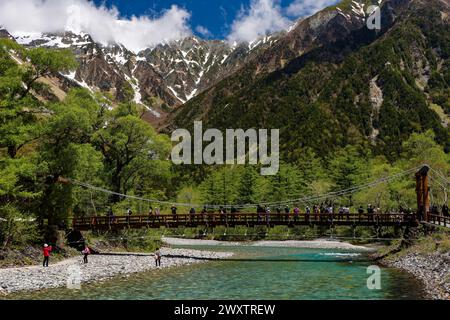 KAMIKOCHI, JAPAN - 24. MAI 2023: Wanderer und Touristen auf Kappabashi mit den schneebedeckten Gipfeln des Kotaka-Gebirges dahinter. Kamikochi, Präfektur Nagano Stockfoto