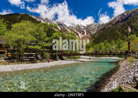 KAMIKOCHI, JAPAN - 24. MAI 2023: Wanderer und Touristen auf Kappabashi mit den schneebedeckten Gipfeln des Kotaka-Gebirges dahinter. Kamikochi, Präfektur Nagano Stockfoto