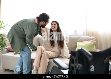 Bärtiger Mann in Hauswäsche, der seiner Frau mit Mobilitätseinschränkung hilft, vom Rollstuhl zur Couch zu kommen Stockfoto