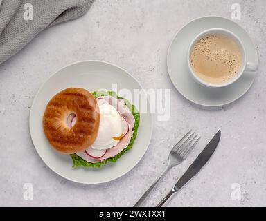 Lebensmittelfotografie von Bagel mit pochiertem Ei, Rettich, Speck, Schinken, Kaffee, Cappuccino, Latte; Romaine-Salat; Sandwich; morgens; in Scheiben geschnitten; Frühstück; brun Stockfoto