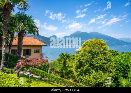 Ein Haus mit rotem Dach liegt auf einem Hügel mit Blick auf das Wasser. Das Haus ist von üppigen grünen Bäumen und Büschen umgeben, die eine ruhige und friedliche Atmosphäre schaffen, Bellagio am Comer See, Italien Stockfoto