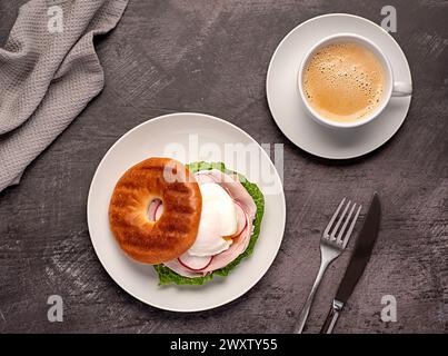 Lebensmittelfotografie von Bagel mit pochiertem Ei, Rettich, Speck, Schinken, Kaffee, Cappuccino, Latte; Romaine-Salat; Sandwich; morgens; in Scheiben geschnitten; Frühstück; brun Stockfoto