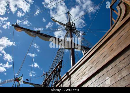 Die hohen Holzmasten des nachgebildeten Karavels Santa Maria vor einem klaren blauen Himmel mit etwas Wolke. Es werden viele Seilkletteranlagen und Seilleitern gesehen. B Stockfoto