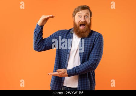 Glücklicher rothaariger bärtiger Kerl, der unsichtbares Produkt in den Händen hält, Studio Stockfoto