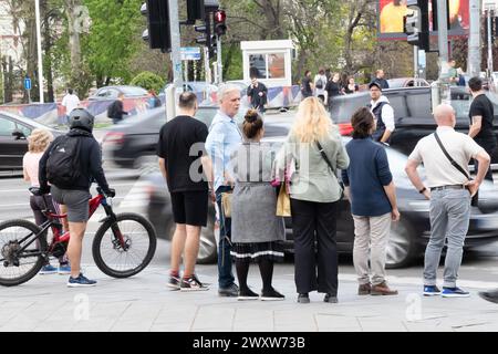 Belgrad, Serbien - 1. April 2024: Menschenmenge, die auf dem Bürgersteig steht und darauf wartet, eine belebte Straße zu überqueren, Rückansicht mit bewegtem Verkehr auf einem Sp Stockfoto