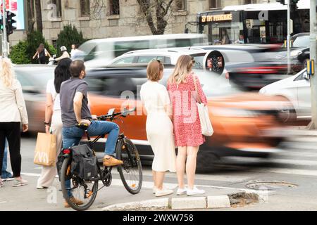 Belgrad, Serbien - 1. April 2024: Menschen, die auf dem Bürgersteig stehen und auf die Überquerung einer belebten Straßenkreuzung warten, Rückansicht mit fahrendem Verkehr verschwimmt Stockfoto